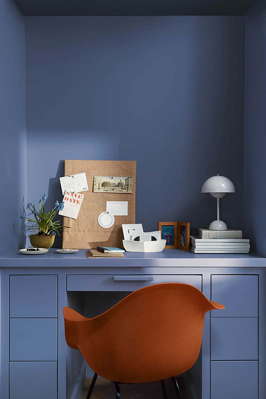 A modern red office chair sits in a home office painted in Blue Nova 825, with built-in shelving, cabinetry and in-set desk topped with a pegboard, plants, books and a modern domed white desk lamp.