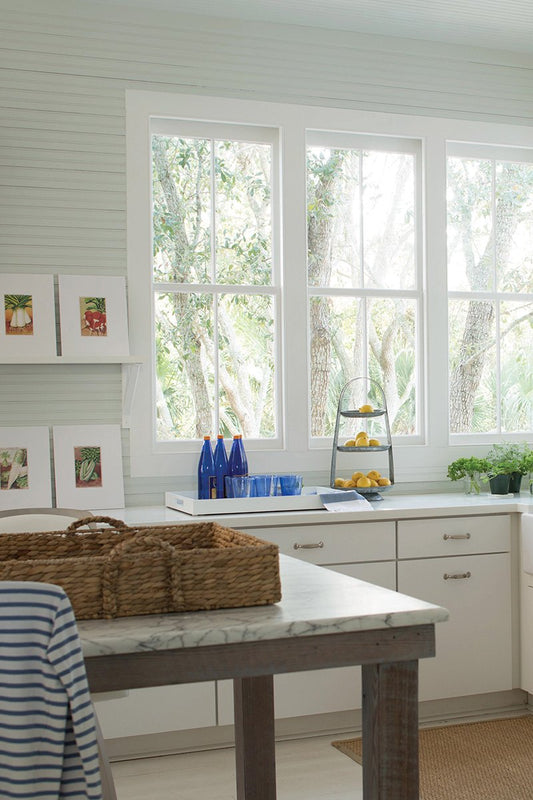 kitchen with big windows, white cabinetry and an island with wicker tray on top